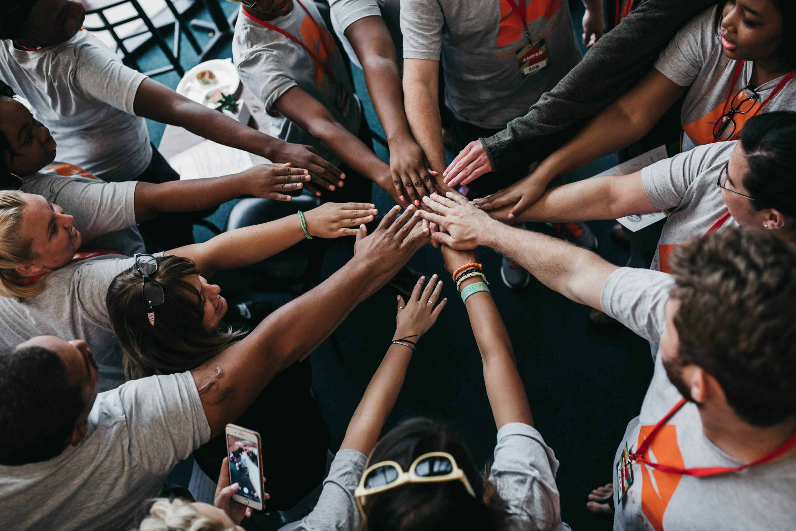 Diverse group of people joining hands together representing team collaboration and collective leadership — Bridging Momentum Waves executive leadership coaching South Florida